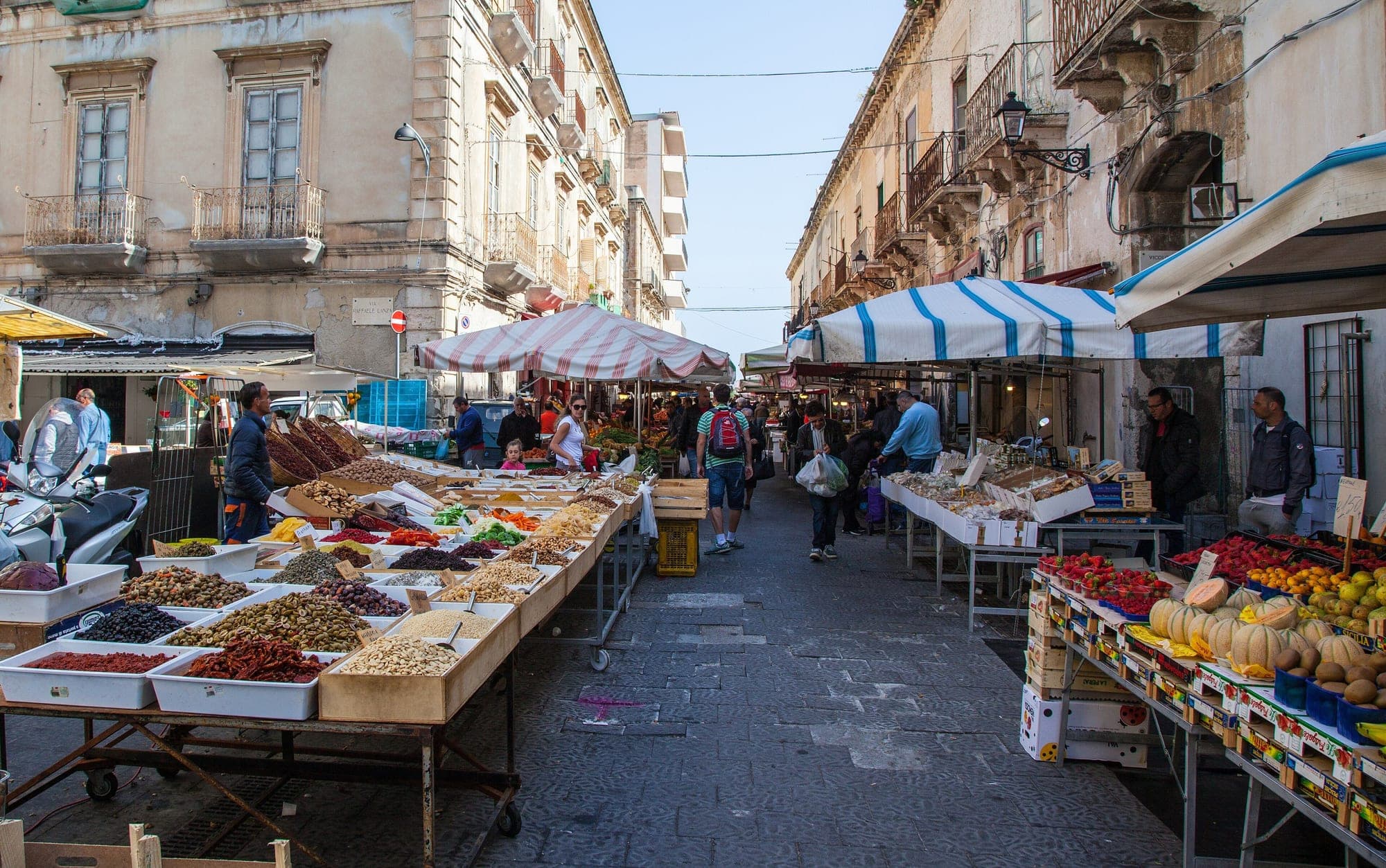 The Ortigia market street between striped awnings, spice stalls and stacked fruit