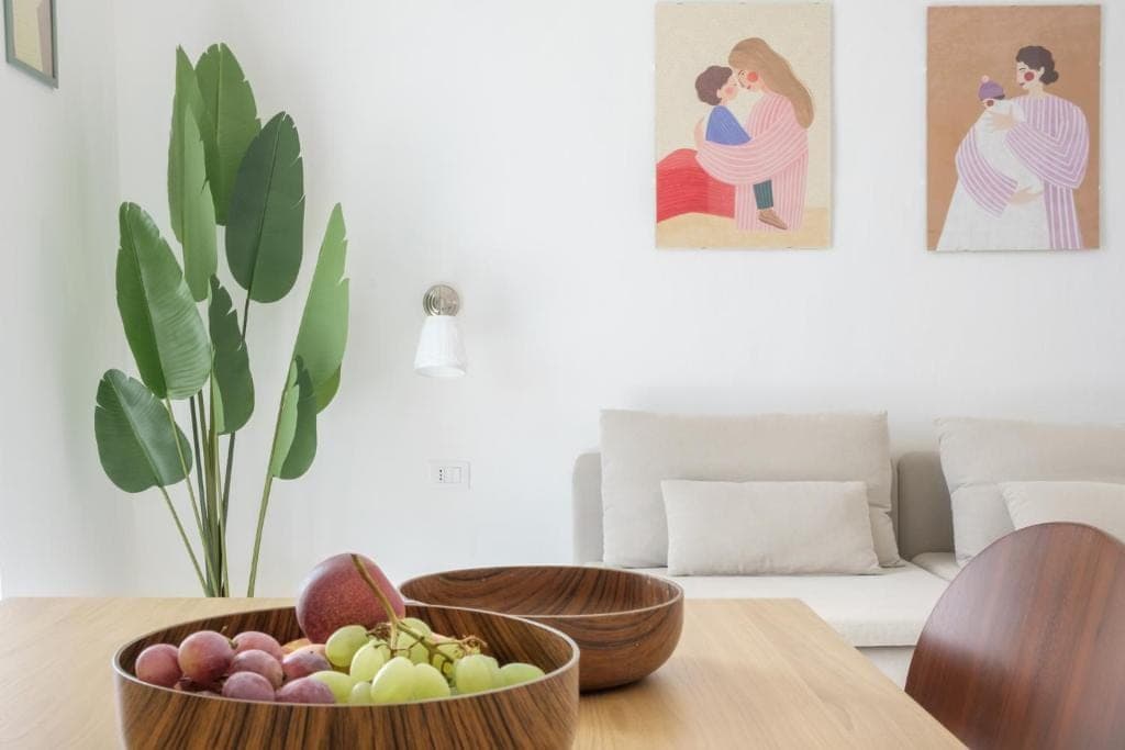 The wooden dining table with fruit in wooden bowls and the pale sofa behind